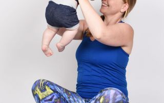 Ein Frau im Schneidersitz hält ihr Kind hoch und lächelt es an